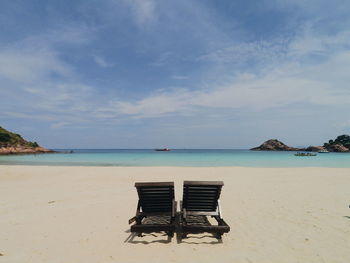 Deck chairs on beach against sky