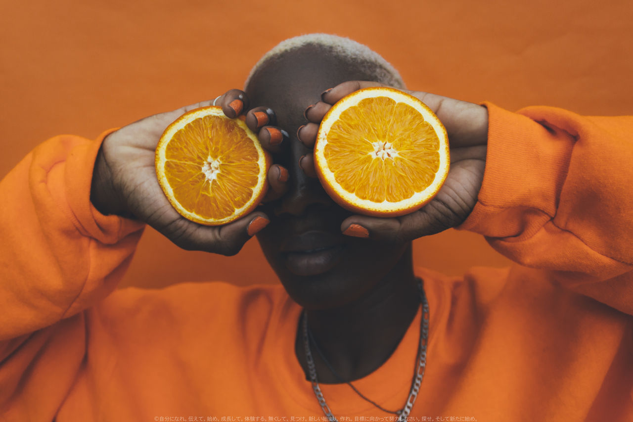 CLOSE-UP OF BOY HOLDING FRUIT ON ORANGE