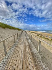 Empty boardwalk leading towards beach against sky