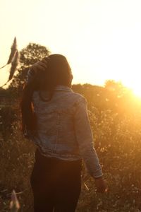Rear view of woman standing on field against sky during sunset