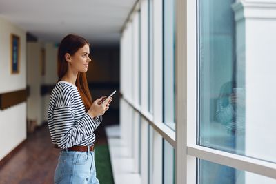 Side view of young woman standing against window