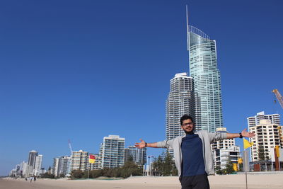 Man with arms outstretched standing against modern buildings