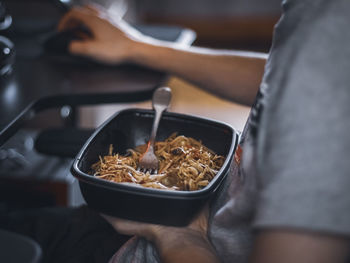 Young caucasian guy gamer holding a black container with wok food during lunch break