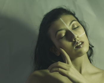 Close-up of shirtless young woman with eyes closed and face paint standing against wall