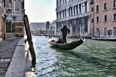 Men in gondola on canal in city against sky
