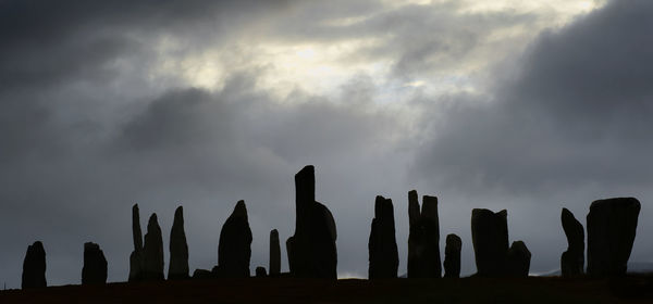 Silhouette rocks on land against storm clouds