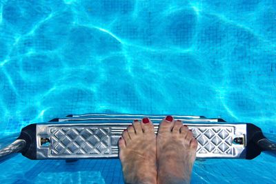 Low section of woman standing on ladder in swimming pool