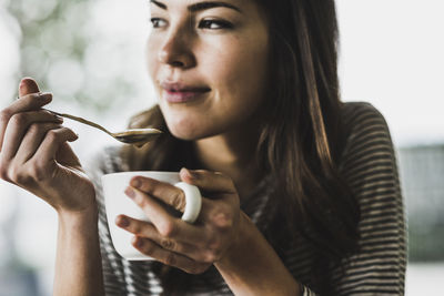 Young woman drinking cappuccino, spooning milk froth