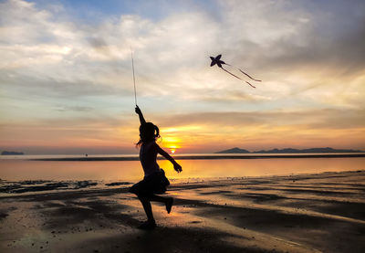 Silhouette girl jumping at beach against sky during sunset