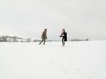 People walking on snow covered field against sky