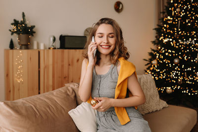 A pretty girl in pajamas rejoices and smiles during the christmas holidays in cozy bedroom interior