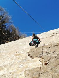 Low angle view of woman climbing wall against clear sky