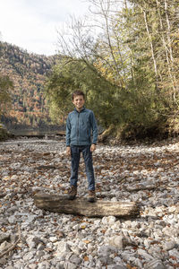 Portrait of boy standing on log in forest