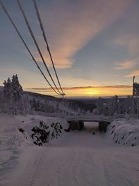 Snow covered land against sky during sunset