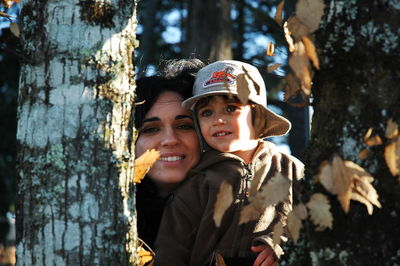 Portrait of happy young woman against tree trunk