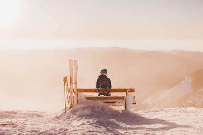 Rear view of man sitting on snow covered mountain