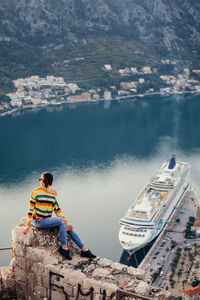 Man sitting on boat in sea by mountain