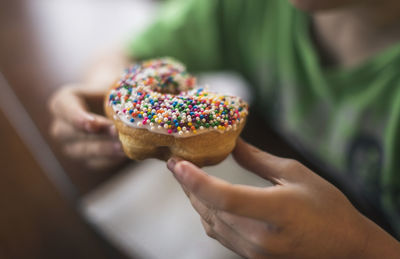 Midsection of boy eating donut while sitting by table at home