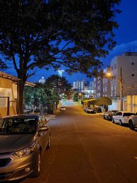 Cars on street by illuminated buildings in city against sky