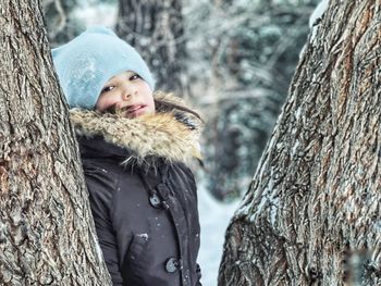 Portrait of boy with snow on tree trunk during winter