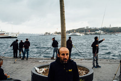 Men standing on sea by city against sky