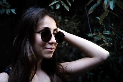 Woman with hand in hair wearing sunglasses against plants