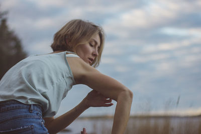 Side view of young woman standing against sky