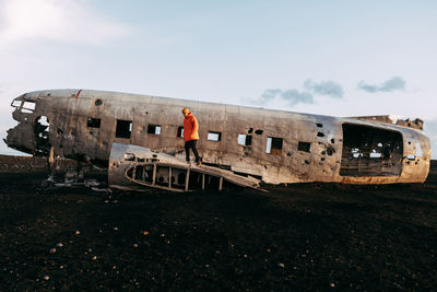 Man standing on abandoned car against sky