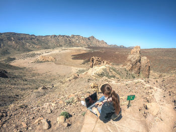 Teenage girl using laptop while sitting on rock at desert