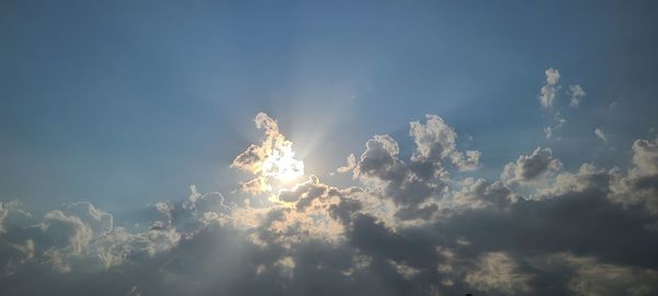 Low angle view of sunlight streaming through clouds