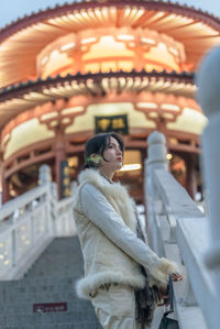 Portrait of young woman standing against building