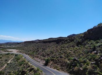 Scenic view of road by mountains against clear blue sky