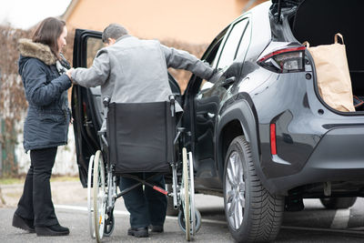 A woman helps aphysical disabled person to get into the car.