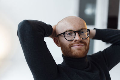 Smiling young businessman with hands behind head in office