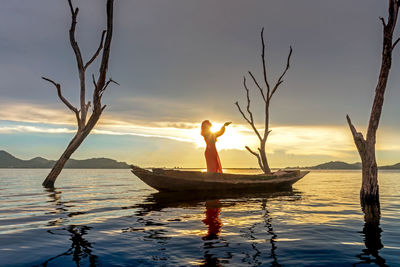 Woman on boat in sea against sky during sunset