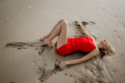 A girl in a red dress lies on the white sea sand