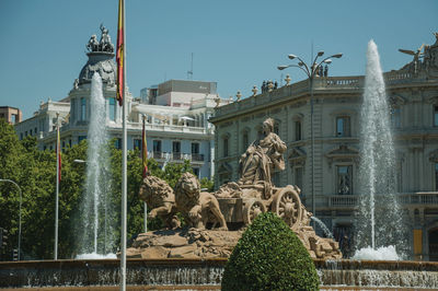 Charming cybele fountain with spanish flags and old buildings on the alcala street in madrid, spain.