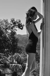 Side view of young woman standing against trees