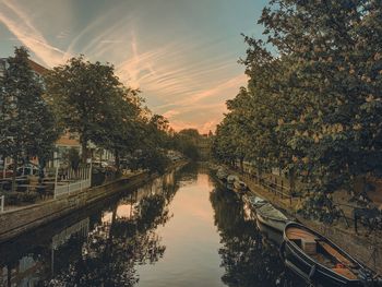Canal amidst trees against sky during sunset