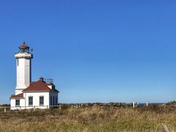 Lighthouse on field against clear blue sky