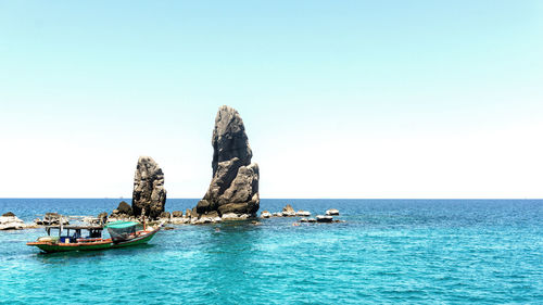 Boat by rock formation in sea against sky