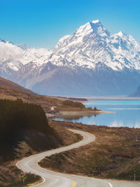 Road by lake against snowcapped mountains