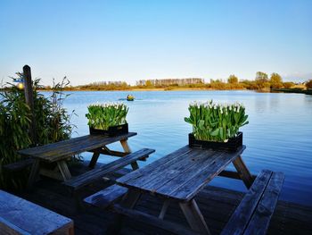 Wooden table by lake against clear sky
