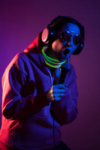 Cyberpunk woman in a hooded hoodie and sunglasses dances against a wall with neon sticks 