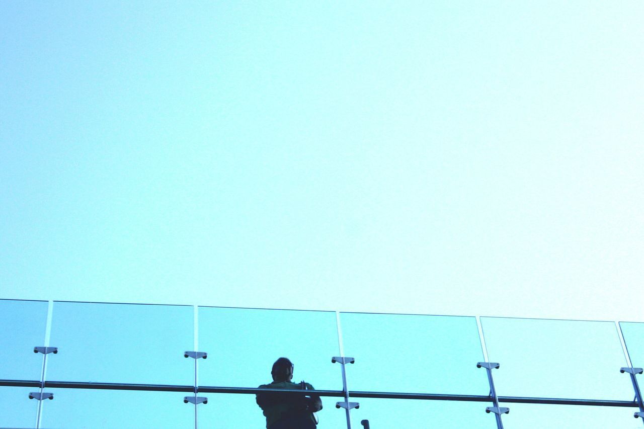 LOW ANGLE VIEW OF MAN PHOTOGRAPHING AGAINST CLEAR BLUE SKY