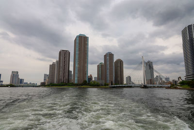 Sea by modern buildings against sky in city