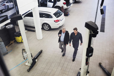 High angle view of senior man discussing with mechanic while walking in auto repair shop