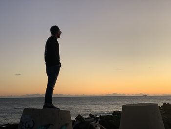 Man standing on beach against sky during sunset