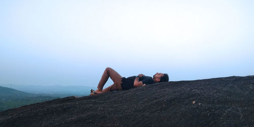 Man lying on mountain peak against clear sky