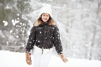 Portrait happy child playing snowballs. girl in warm clothes has fun with snow in winter forest